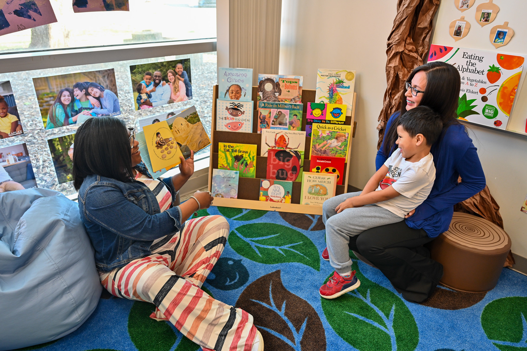 An image of a teach sitting on the floor reading a children's book to a student