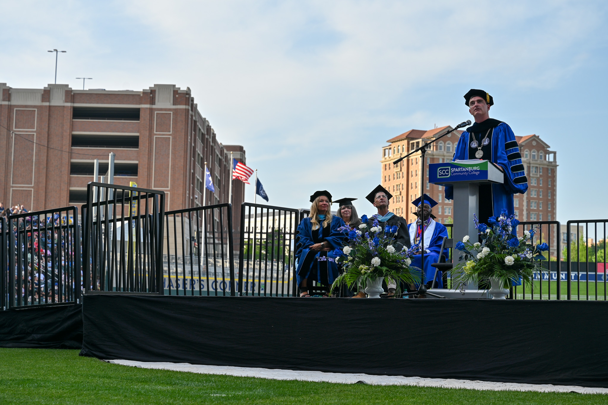 SCC Leadership at Graduation sit onstage as Dr. Mikota delivers a speech