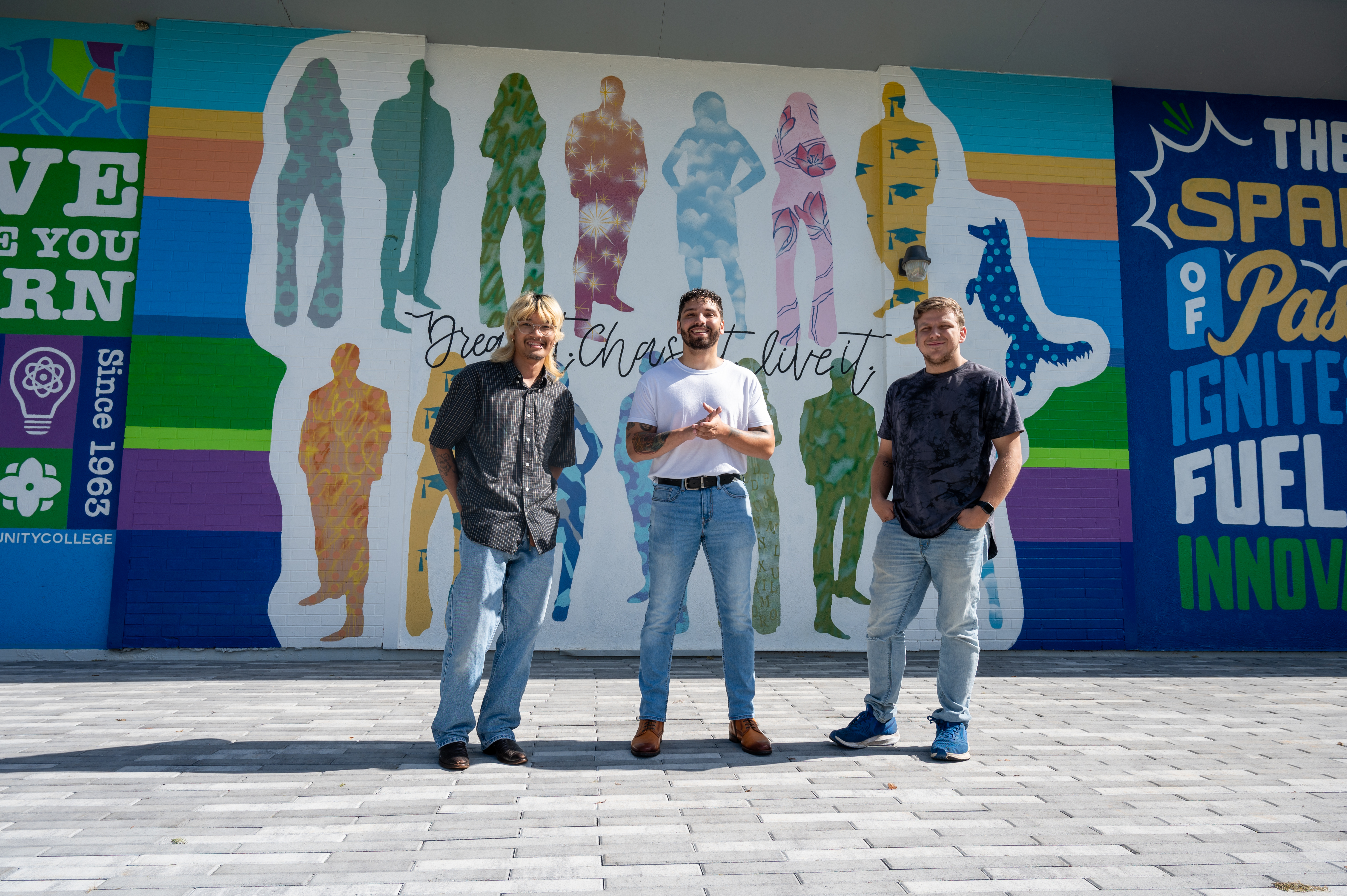 Three students posing in front of a painted wall